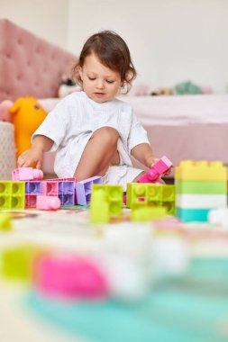 Beyaz yatak odasında renkli oyuncaklarla oynayan tatlı bir kız.