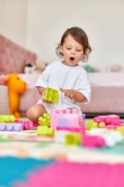 Şaşırmış bebek evde renkli oyuncaklarla oynuyor.