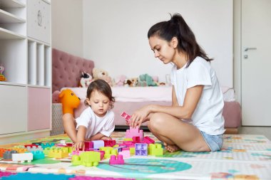 Sevimli küçük kız ve annesi çocuk odasında renkli bloklarla oynuyorlar, birlikte eğleniyorlar.