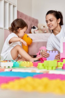 Sevimli kız ve sevgili annesi renkli küplerden kule inşa edip birlikte eğleniyorlar.