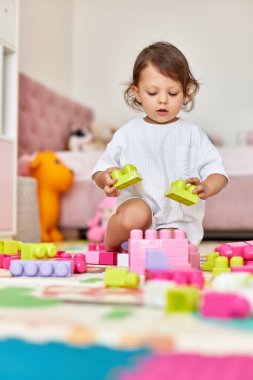 Beyaz pembe yatak odasında renkli parlak küplerle oynayan tatlı bir kız.