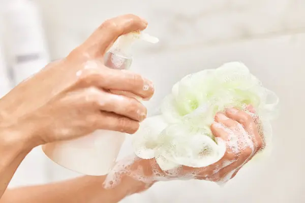 stock image female hands applying liquid soap shower gel from white cosmetic bottle on sponge in bathroom