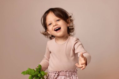 Çok heyecanlı gülümseyen kız bej arka planda taze yeşil salata tutuyor. sağlıklı bebek maması.