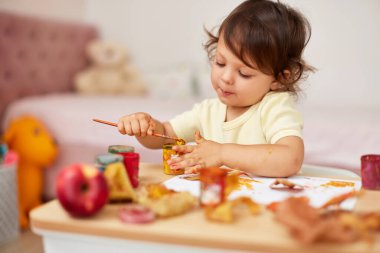 happy little child girl painting autumn leaves. baby girl drawing leaves in yellow paint clipart