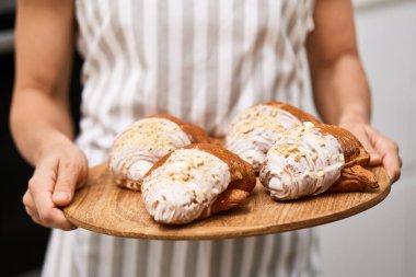 Kadın fırıncı elinde ahşap tepsiyle taze pişmiş altın kruvasan tutuyor.