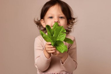 Bej arka planda taze yeşil salata tutan gülümseyen kız çocuğu. Salataya odaklan