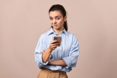 Cep telefonu tutan şüpheli güzel bir kadın bej arka plandaki kameraya bakıyor..