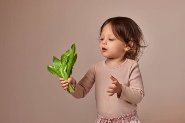 Bej arka planda taze yeşil salata tutan tatlı bir kız çocuğu. sağlıklı bebek maması.