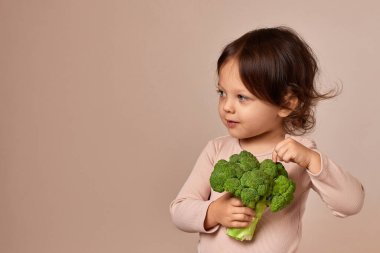 Gülümseyen kız bej arka planda taze yeşil brokoli tutuyor. sağlıklı bebek maması. Boşluğu kopyala