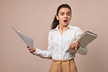 Beyaz gömlekli iş kadınının elinde bej arkaplanlı belgelerle klasörler tutmasına şaşırdım.