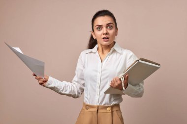 Beyaz gömlekli iş kadını elinde bej arkaplanlı belgeler olan klasörler tutuyor.