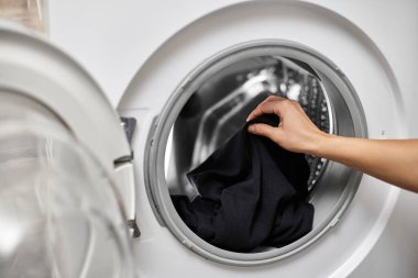 Kadın çamaşır makinesine siyah pamuk koyuyor, yakın plan.