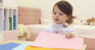 Küçük kız masada renkli kağıtları makasla kesiyor. çocuk yaratıcılığı.