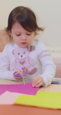 Küçük kız masada renkli kağıtları makasla kesiyor. çocuk yaratıcılığı.