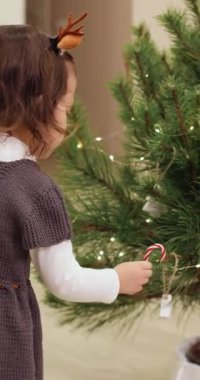 Sevimli küçük kız Noel ağacını oyuncak şekerlerle süslüyor.