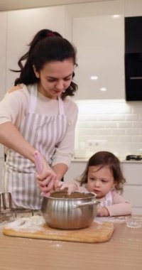 Gülümseyen anne ve önlüklü küçük tatlı kız mutfakta hamur hazırlıyor, kurabiye pişiriyor.