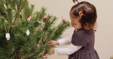 Sevimli küçük kız Noel ağacını oyuncak şekerlerle süslüyor.