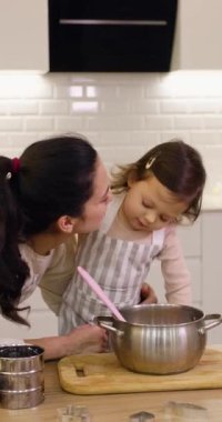 Güzel anne ve önlüklü küçük tatlı kızı mutfakta hamuru hazırlıyorlar, kurabiye pişiriyorlar.