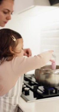 Anne ve önlüklü küçük kızı mutfakta yemek pişiriyorlar.