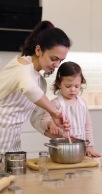 Güzel anne ve önlüklü küçük tatlı kızı mutfakta hamuru hazırlıyorlar, kurabiye pişiriyorlar.