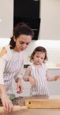 Güzel anne ve önlüklü küçük tatlı kızı mutfakta hamuru hazırlıyorlar, kurabiye pişiriyorlar.
