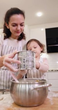 Anne ve küçük kız önlük giyip mutfakta birlikte pişirmek için un seçiyorlar.