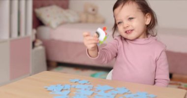 Odanın ahşap masasında yapboz parçaları birleştiren sevimli küçük kız çocuğu, çocuk gelişimi.