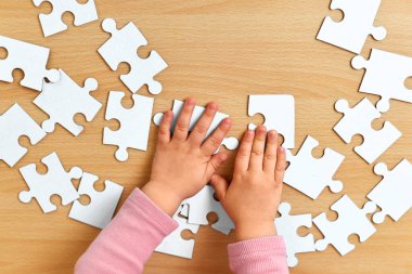 Küçük çocuğun elleri ahşap masaya mavi yapboz diziyor, üst görünüm, çocukların gelişimi.