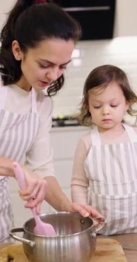 Güzel anne ve önlüklü küçük tatlı kızı mutfakta hamuru hazırlıyorlar, kurabiye pişiriyorlar.