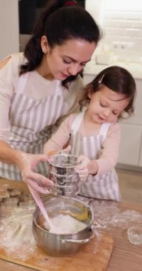 Anne ve küçük kız önlük giyip mutfakta birlikte pişirmek için un seçiyorlar.