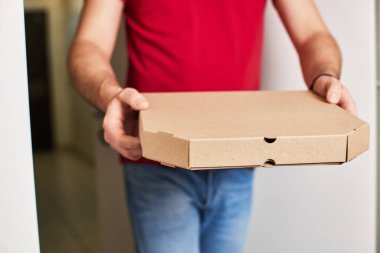 Kırmızı tişörtlü teslimatçının elleri yemek siparişi veriyor ve elinde pizza kutusu tutuyor..
