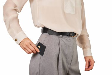 Resmi kıyafetli bir kadın, siyah prim kredi kartını beyaz arka planda gri pantolon cebine koyuyor. Para finans