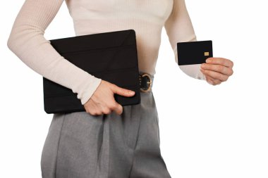 Beyaz bluzlu ve gri pantolonlu kadın beyaz arka planda kredi kartı ve dijital tablet kullanıyor.