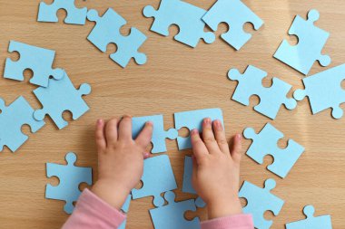 Küçük çocuğun elleri ahşap masa üzerinde mavi yapboz parçaları birleştiriyor, üst görünüm, eğitim kavramı.