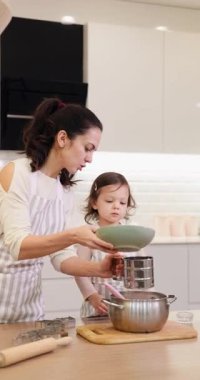 Anne ve küçük kız önlük giyip un seçiyorlar modern mutfakta birlikte pişirmek için.