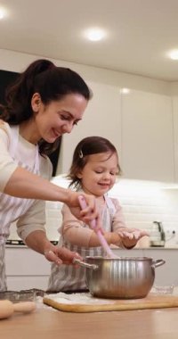 Gülümseyen anne ve önlüklü küçük tatlı kız mutfakta hamur hazırlıyor, kurabiye pişiriyor.