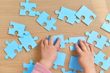 Küçük çocuğun elleri ahşap masaya mavi yapboz diziyor, üst görünüm, çocukların gelişimi.