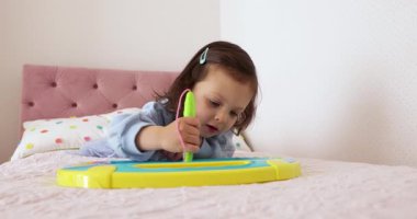 Küçük çocuk yatakta manyetik silinebilen tahtaya resim çiziyor.