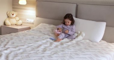 Bebek bebek yatakta oyuncak bebekle oynar, bebek saçlarını tarar.