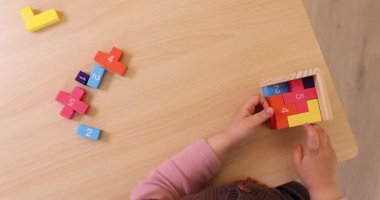 Küçük kız çocuğunun yakın plan fotoğrafları masanın üstünde 3D bulmaca topluyor.