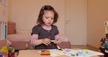 Evdeki beyaz kağıda kurşun kalemle resim çizen küçük şirin bir kız çocuğu. Yaratıcı aktivite.