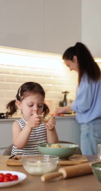 Küçük kız mutfakta hamur yoğuruyor, kız çocuğu annesine yemek pişirmesinde yardım ediyor.