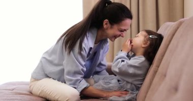 Mutlu kaygısız anne evdeki kanepede gülen küçük kızını gıdıklıyor. Aile eğleniyor.