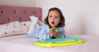 Küçük çocuk yatakta manyetik silinebilen tahtaya resim çiziyor.