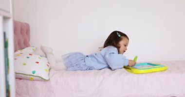 Küçük çocuk yatakta manyetik silinebilen tahtaya resim çiziyor.