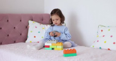 Küçük kız yatakta inşaatçılık oynuyor. Çocuk oyuncak tuğlalarla inşa ediyor. yapıcı küpleri
