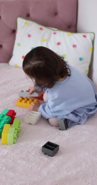 Küçük kız yatakta inşaatçılık oynuyor. Çocuk oyuncak tuğlalarla inşa ediyor. yapıcı küpleri