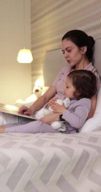 Anne yatak odasında küçük kızına masal okuyor. Çocuklar için eğitim.