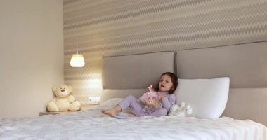 Bebek bebek yatakta oyuncak bebekle oynar, bebek saçlarını tarar.