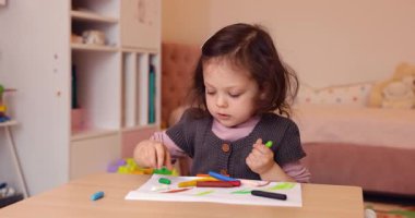 Evdeki beyaz kağıda kurşun kalemle resim çizen küçük şirin bir kız çocuğu. Yaratıcı aktivite.